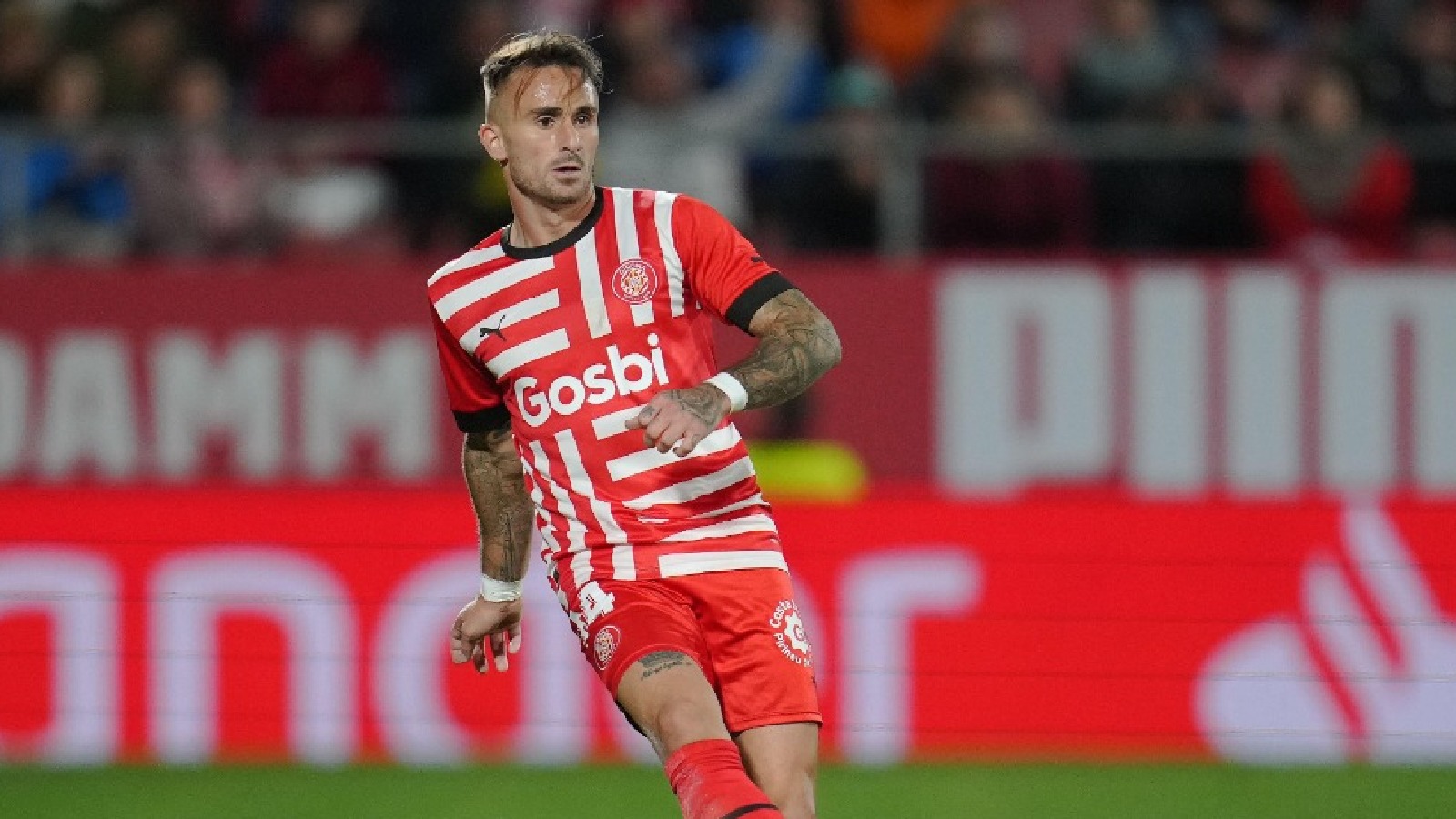  Aleix Garcia Bayer Leverkusen player wearing a red and white striped shirt with the word 'Gosbi' as a sponsor on the front is on the pitch playing in a football match.